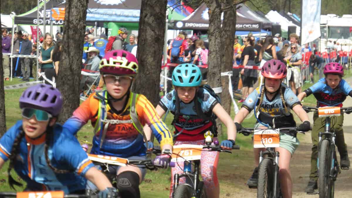 Five cyclists in a row racing with bike race village in background
