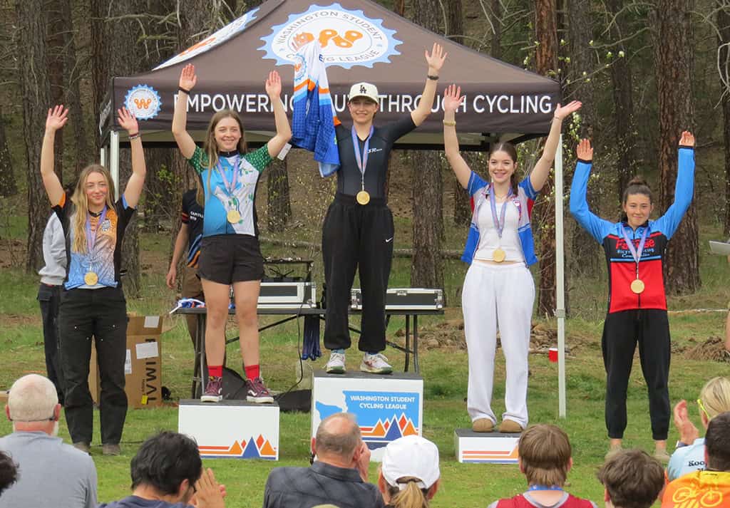 Five cyclist winners on podium with medals in front of Washington Student Cycling League tent