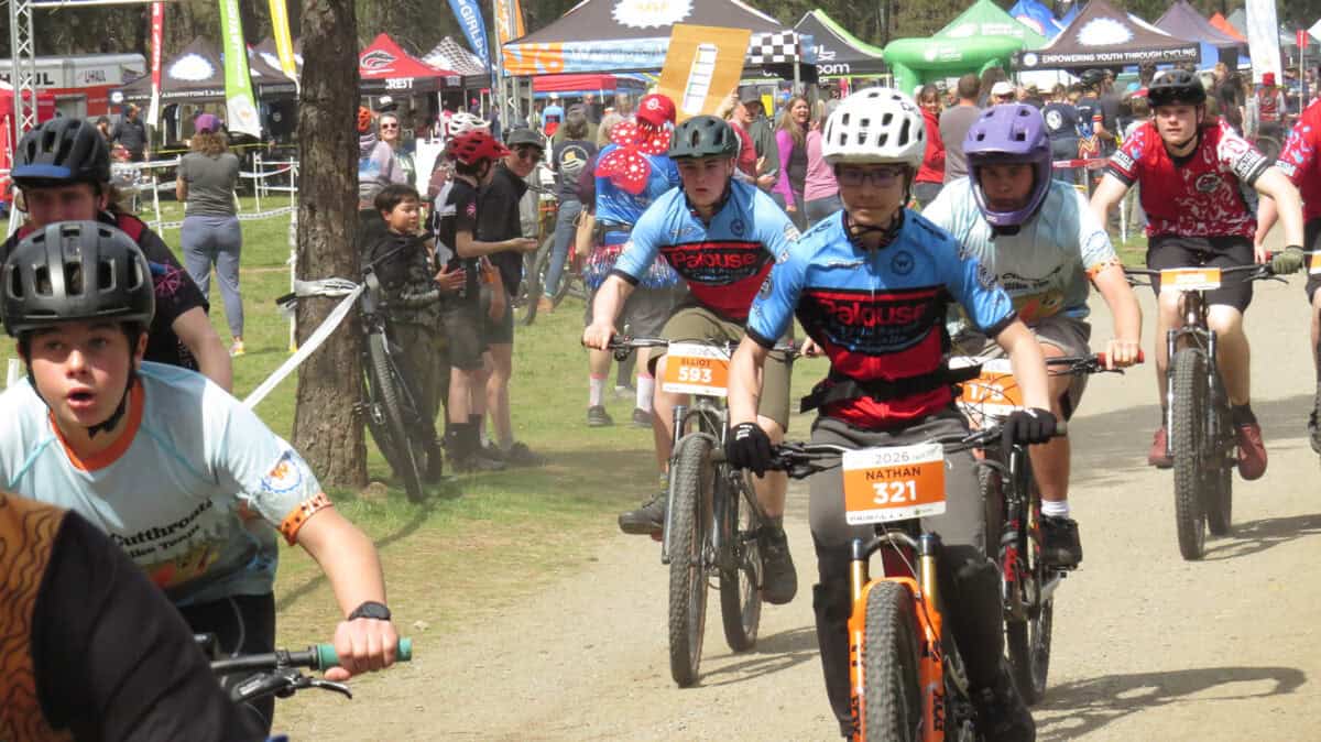 Cyclists in race right after the start with spectators and race village tents in background