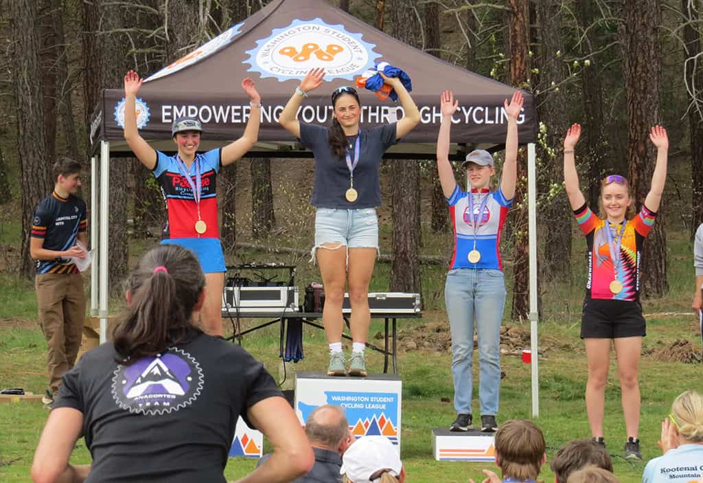 Four cyclist winners on podium with medals in front of Washington Student Cycling League tent